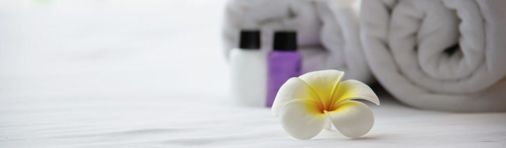 Hotel towel and shampoo and soap bath bottle set on white bed with plumeria flower decorated - relax vacation at the hotel resort concept